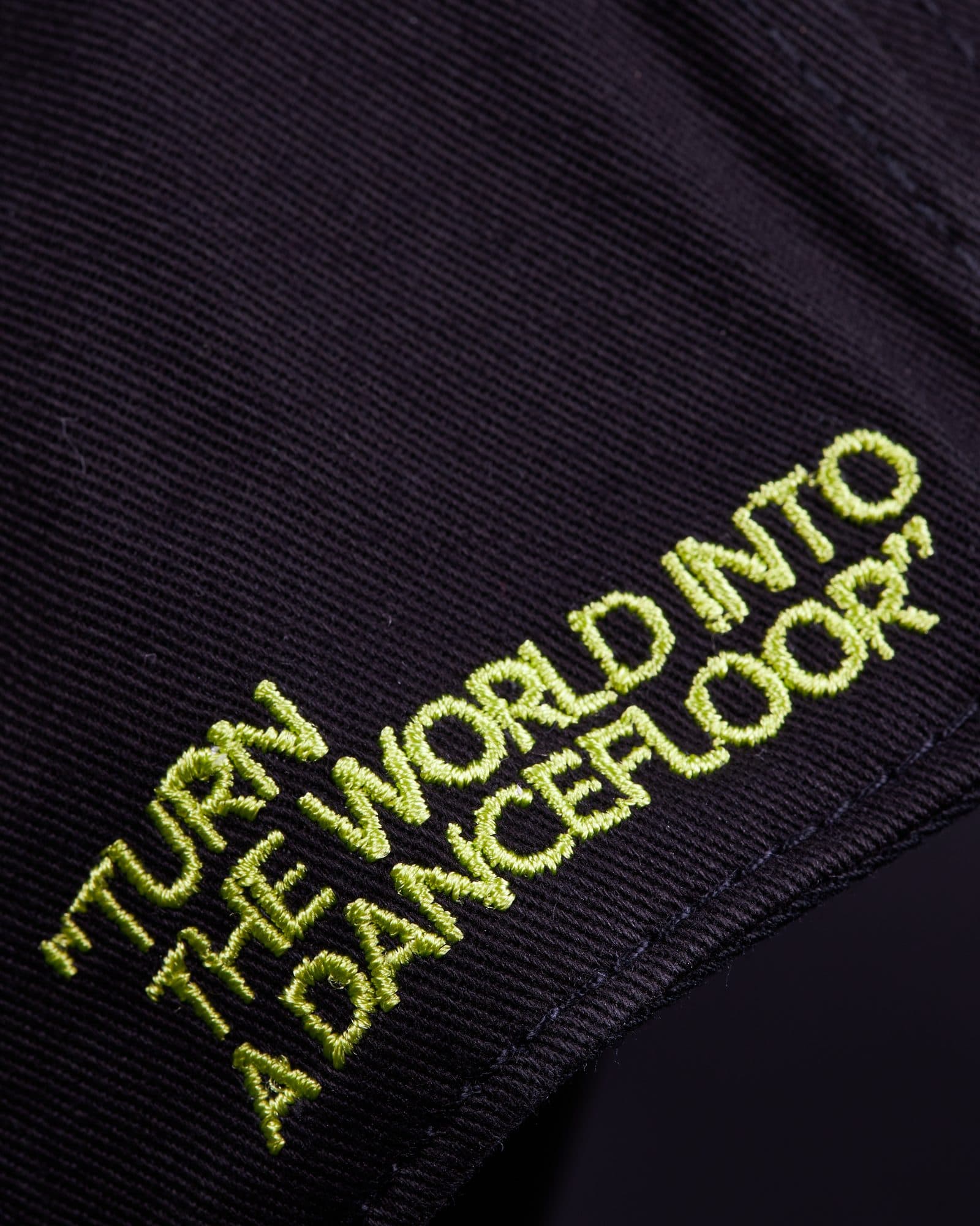 Close-up of the side of the black cap, with TURN THE WORLD INTO A DANCEFLOOR in quotation marks embroidered in lime green capitals over three slanted lines.