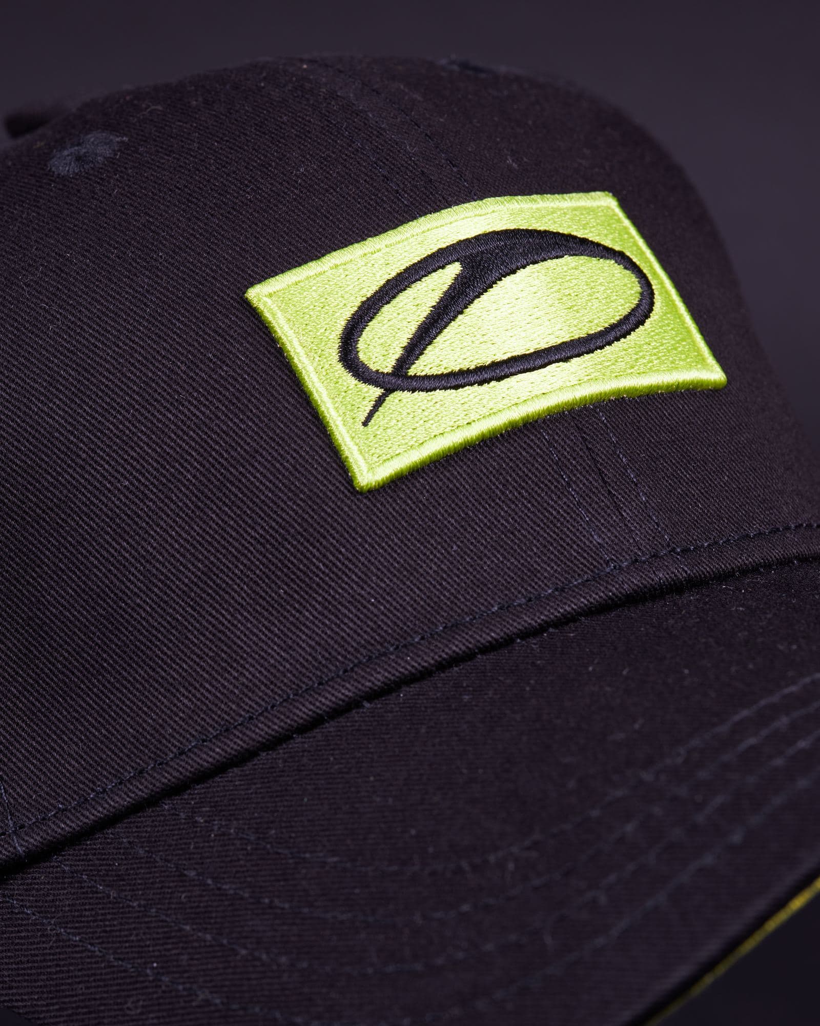 Close-up of the front of a black twill cap with a lime green embroidered patch bearing the A State of Trance logo in black, above a brim with rows of stitching and a thin lime green edge underneath.