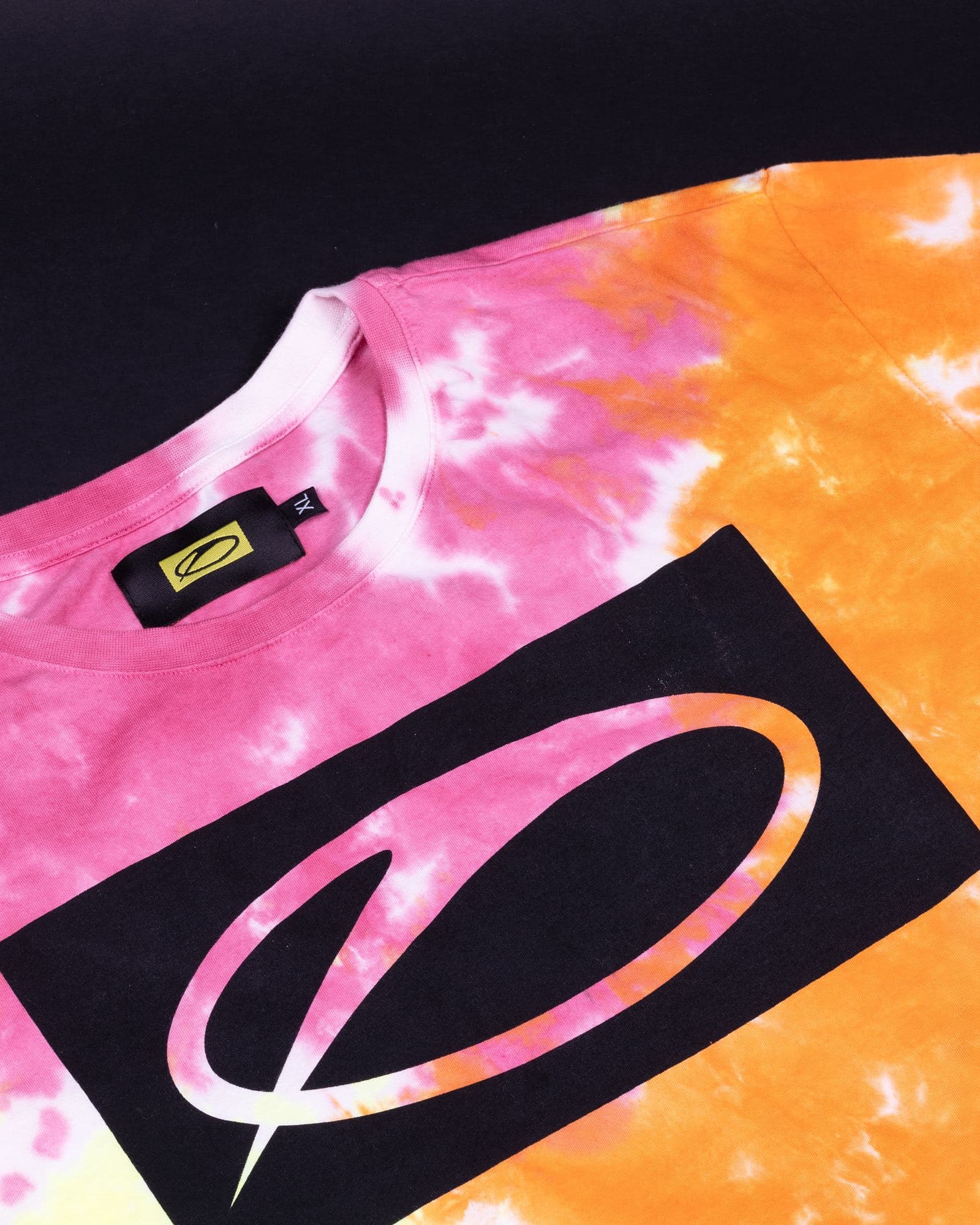 A pink, orange and white tie-dye T-shirt on a dark ground, with a black woven neck label showing the A State of Trance logo on yellow and a large black rectangle printed across the chest, the logo left open in it in the colours of the dye.
