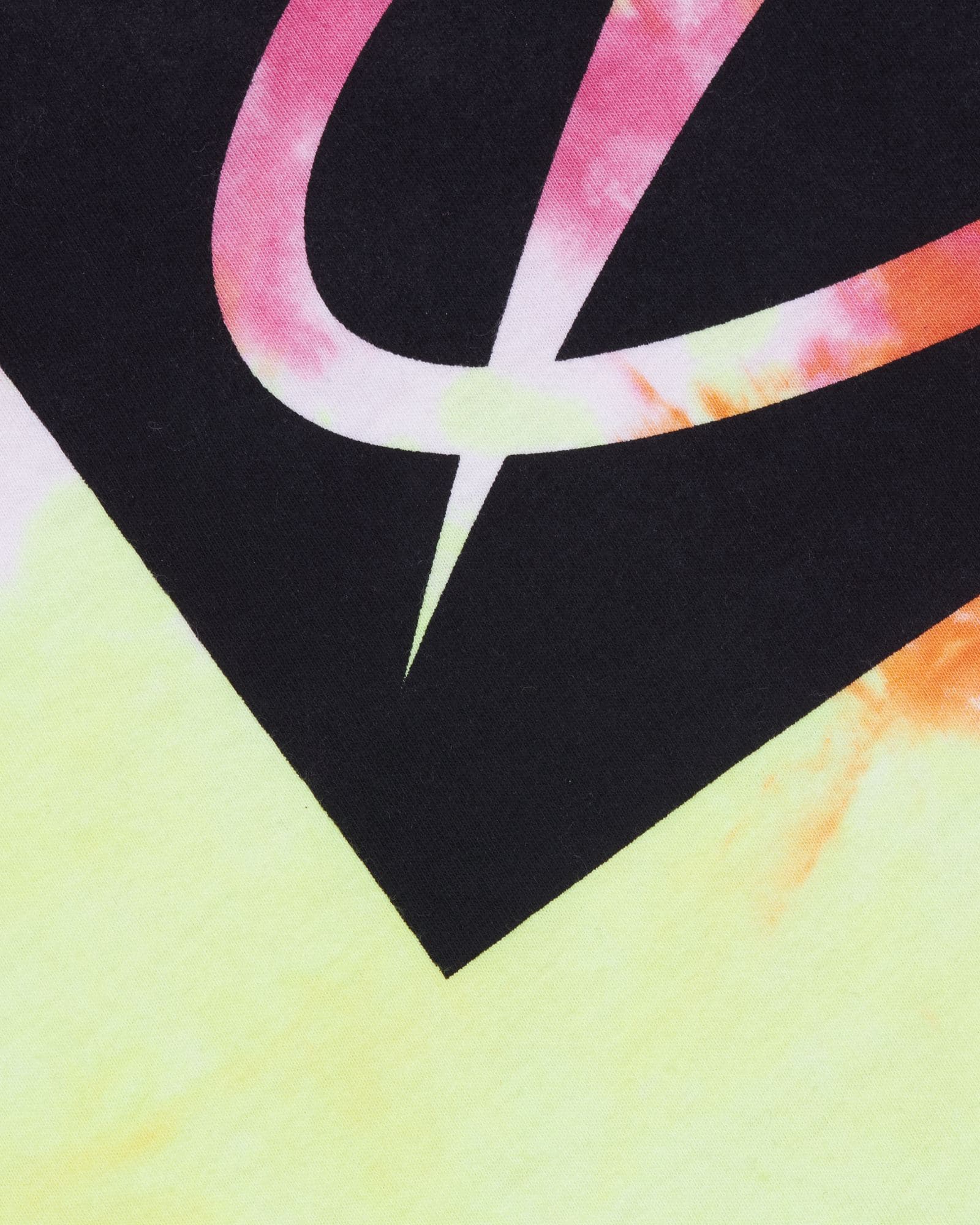 Close-up of the lower corner of the black chest print on the tie-dye T-shirt, with the pointed tail of the A State of Trance logo left open in pink, white and pale yellow, above pale yellow fabric with pink and orange at the edges.