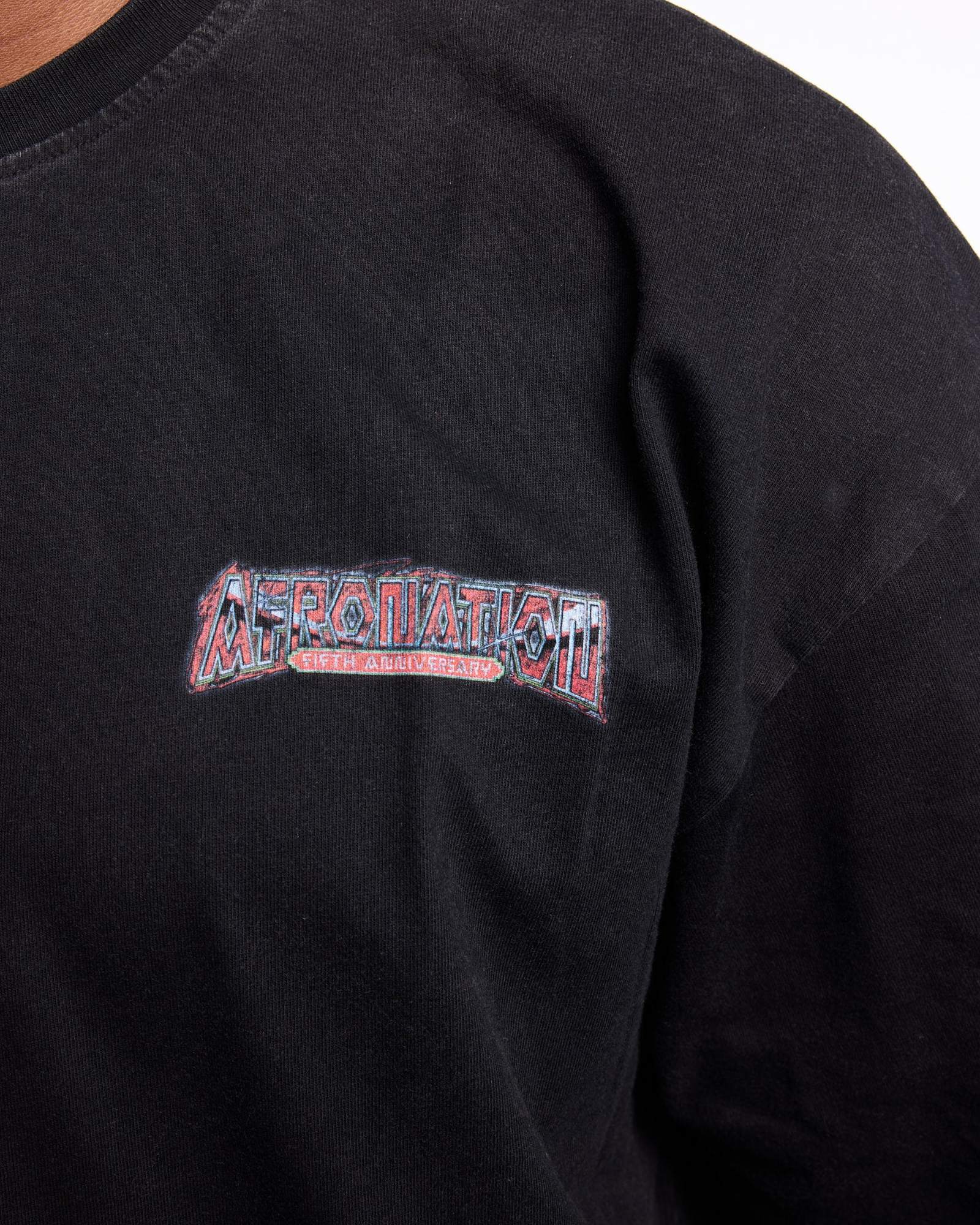 Close-up of the chest of a washed black T-shirt with a small print of AFRO NATION in red and white letters outlined in pale blue, and FIFTH ANNIVERSARY on a red banner edged in green.