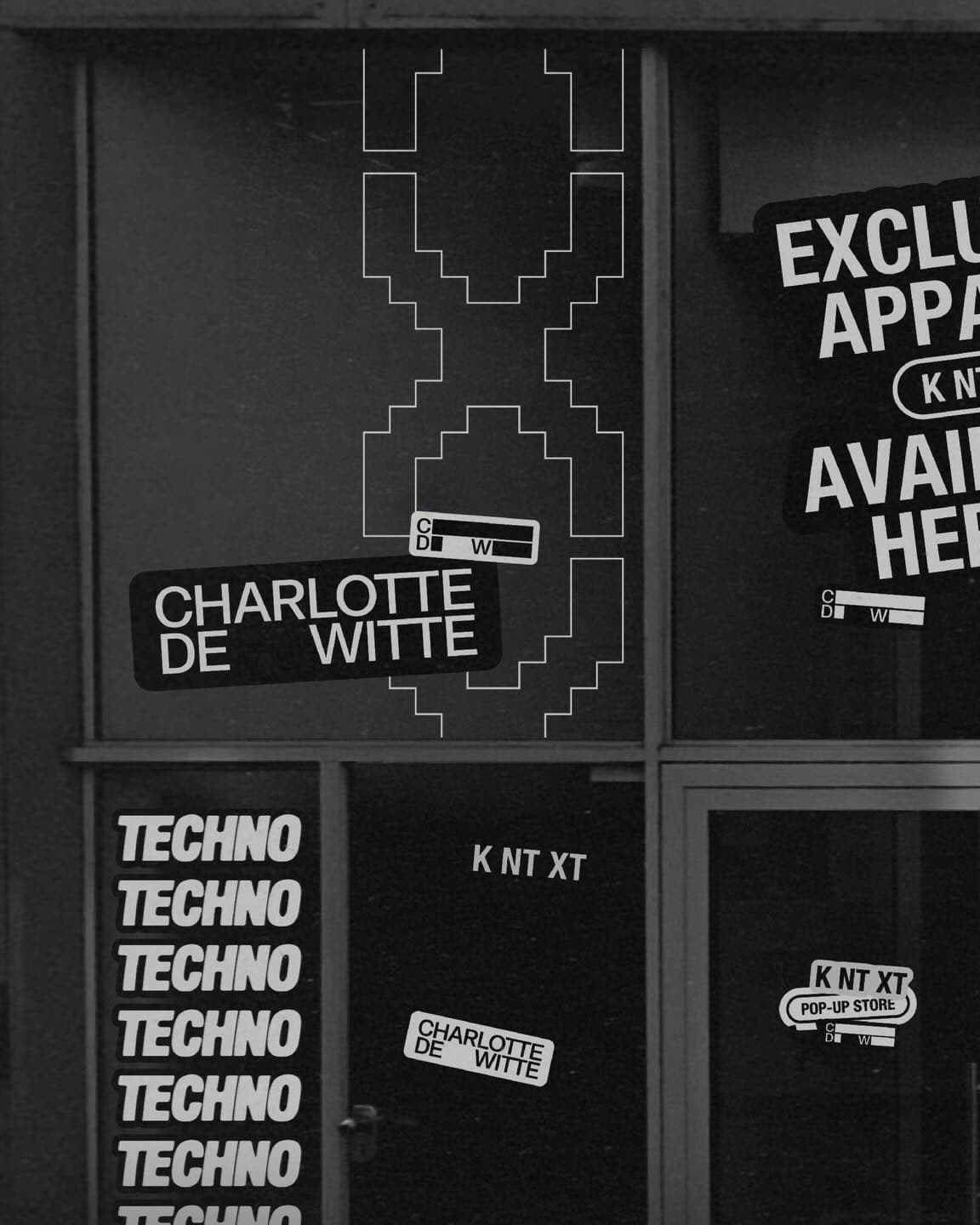 Black and white shop window of a KNTXT pop-up store with stickers on the glass: CHARLOTTE DE WITTE, a large outlined pixel X, TECHNO stacked down one pane, KNTXT, a sticker reading EXCLU, APPA and AVAI cut off at the edge, and a KNTXT POP-UP STORE sticker on the door.