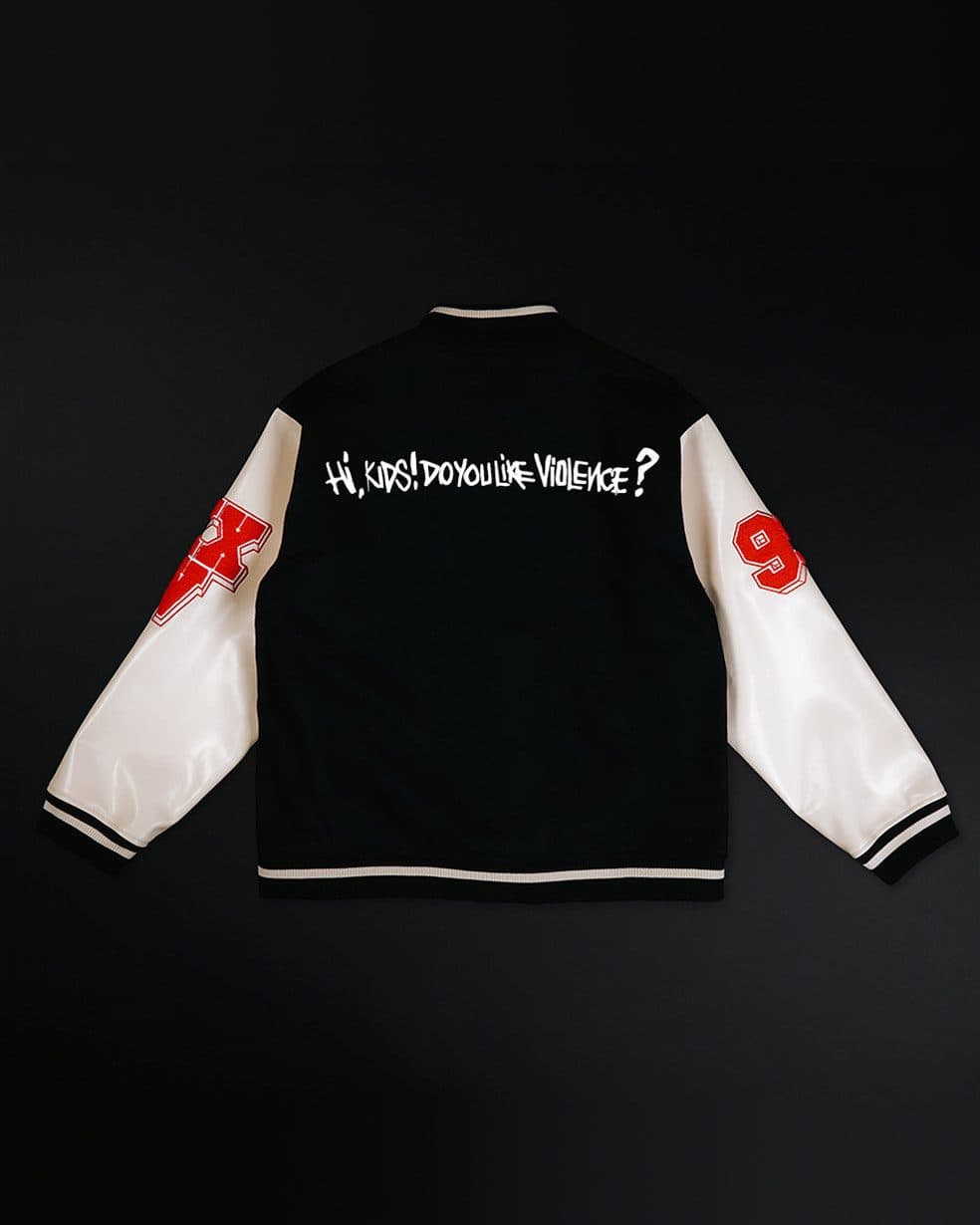 Back of the Slim Shady 25 varsity jacket on a near-black ground: black with cream sleeves, a red X patch on one sleeve and a red 9 on the other, black and cream striped ribbing at the collar, cuffs and hem, and a hand-lettered line in white across the back reading Hi, KIDS! DO YOU LIKE VIOLENCE?