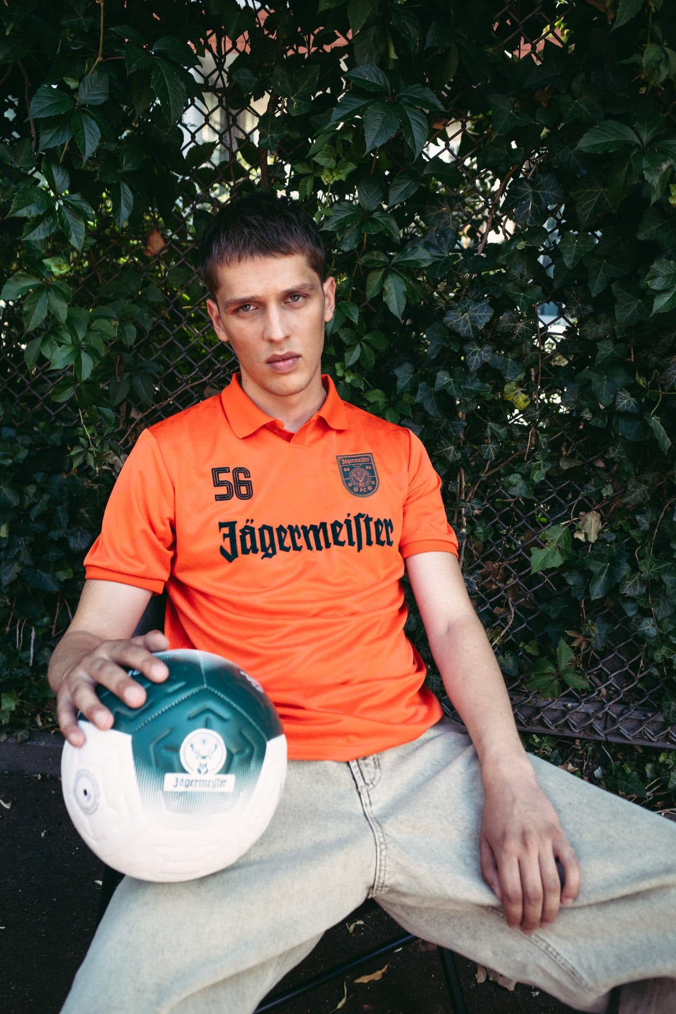Front of an orange Jägermeister football shirt with the 56 and the crest, worn with a white and green Jägermeister football.