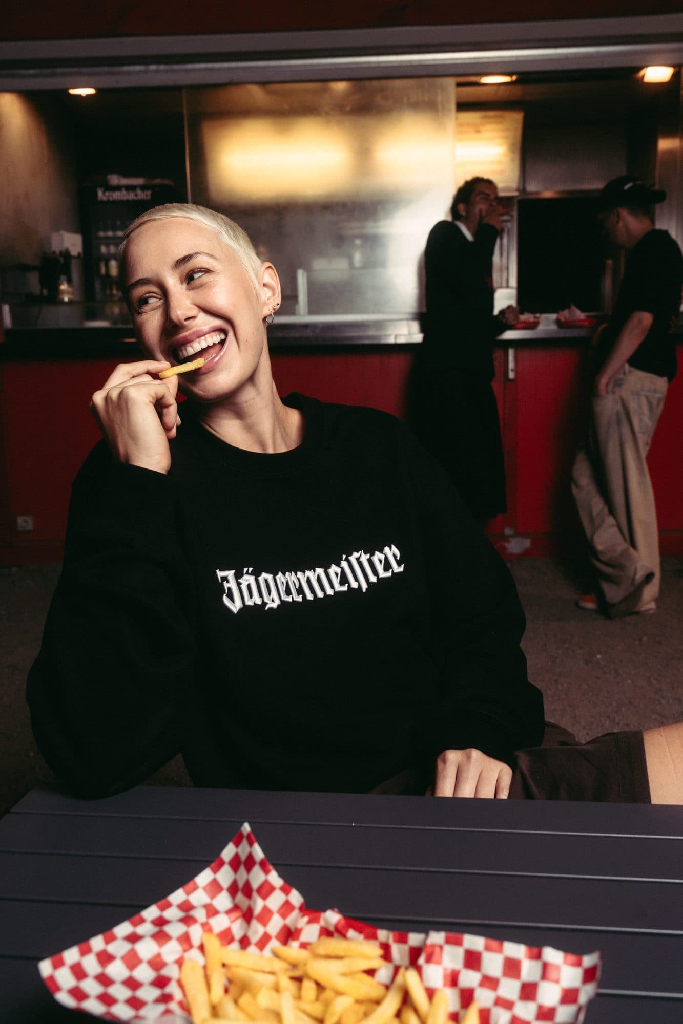Black Jägermeister crewneck with white gothic lettering, at a snack bar.