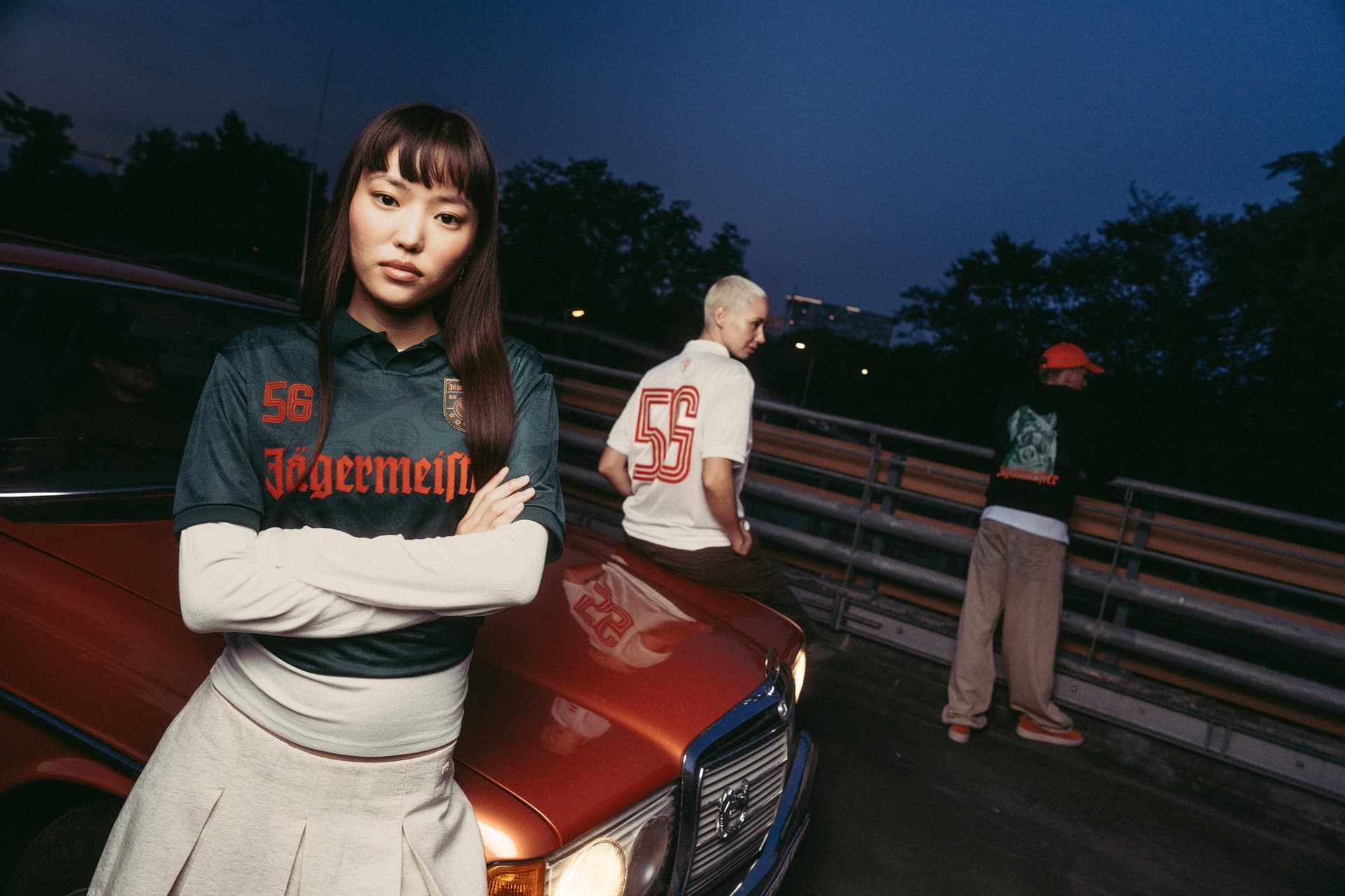 Green Jägermeister football shirt with a cream collar, at dusk beside an orange car.