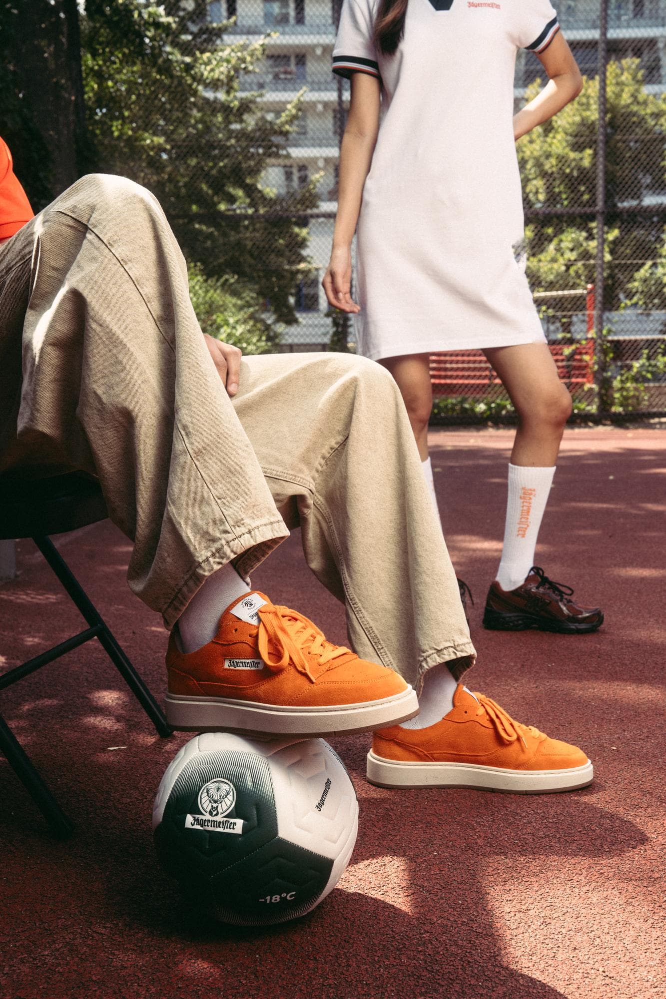 Orange suede sneakers and a white and green Jägermeister football on a red court.