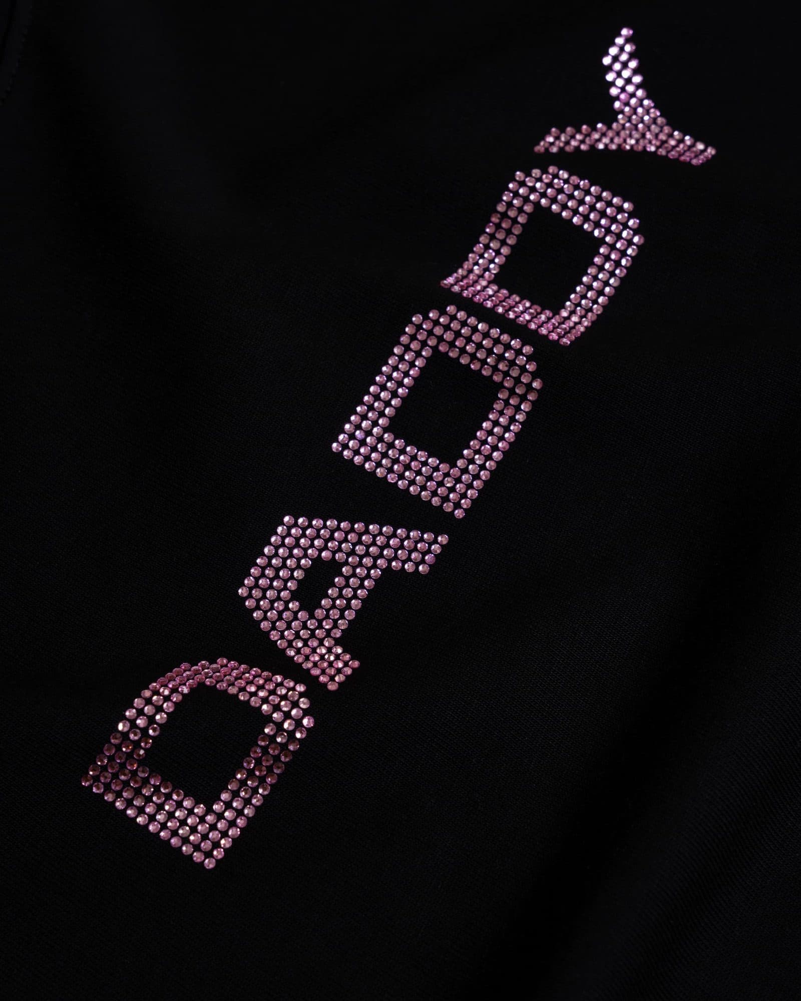 Close-up of DADDY in pink rhinestones running diagonally up across black T-shirt fabric.