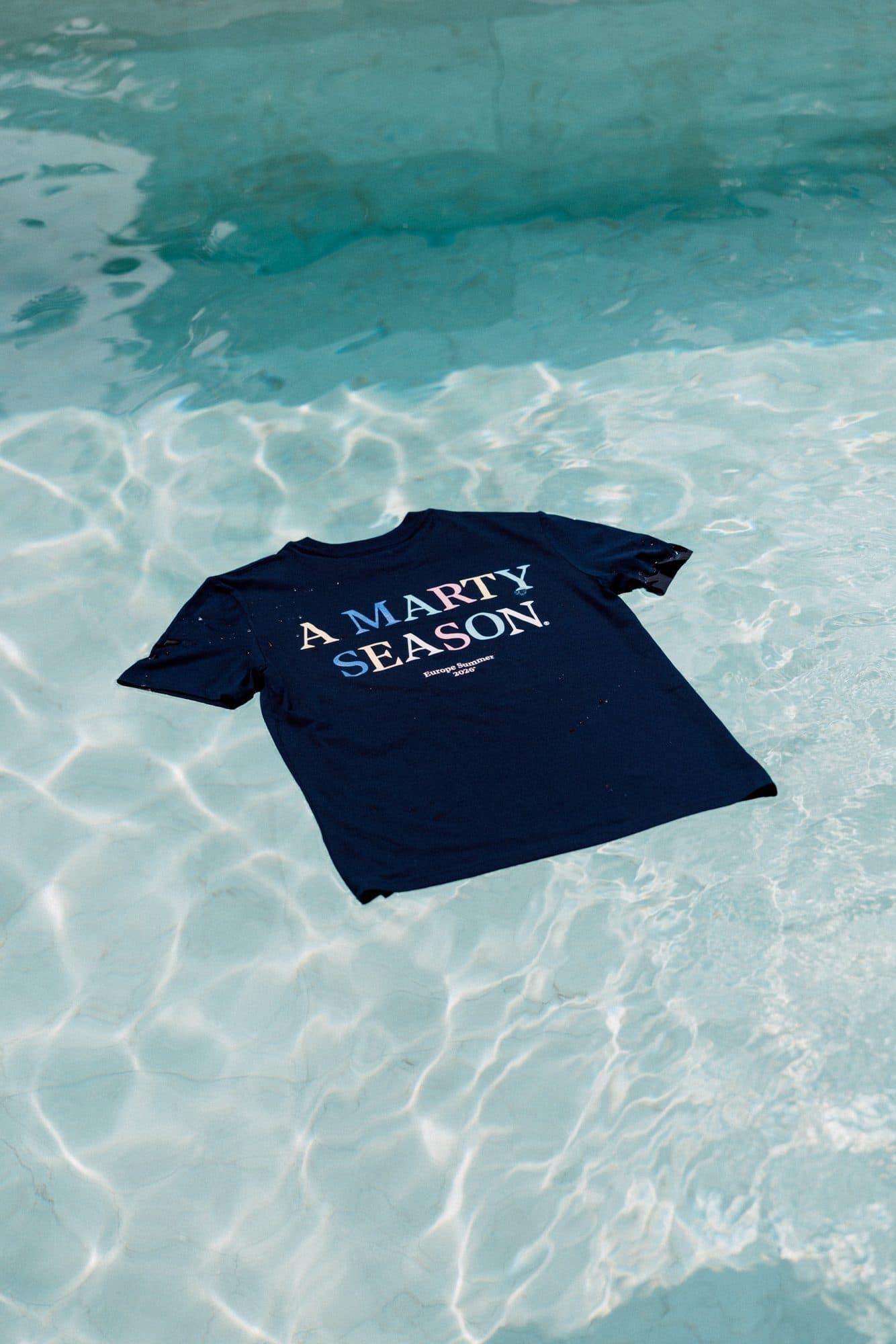 A navy A Marty Season T-shirt floating in a swimming pool.