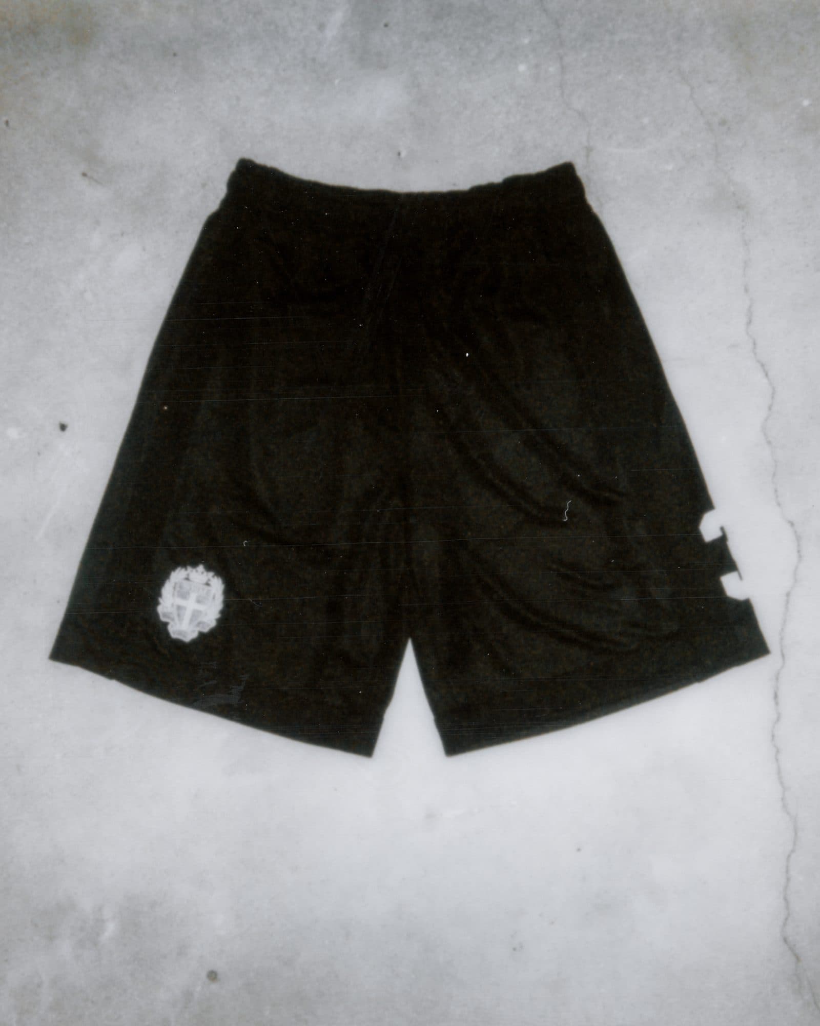 Black shorts with a white crest on one leg and part of a white number 3 at the side, flat on a concrete floor.