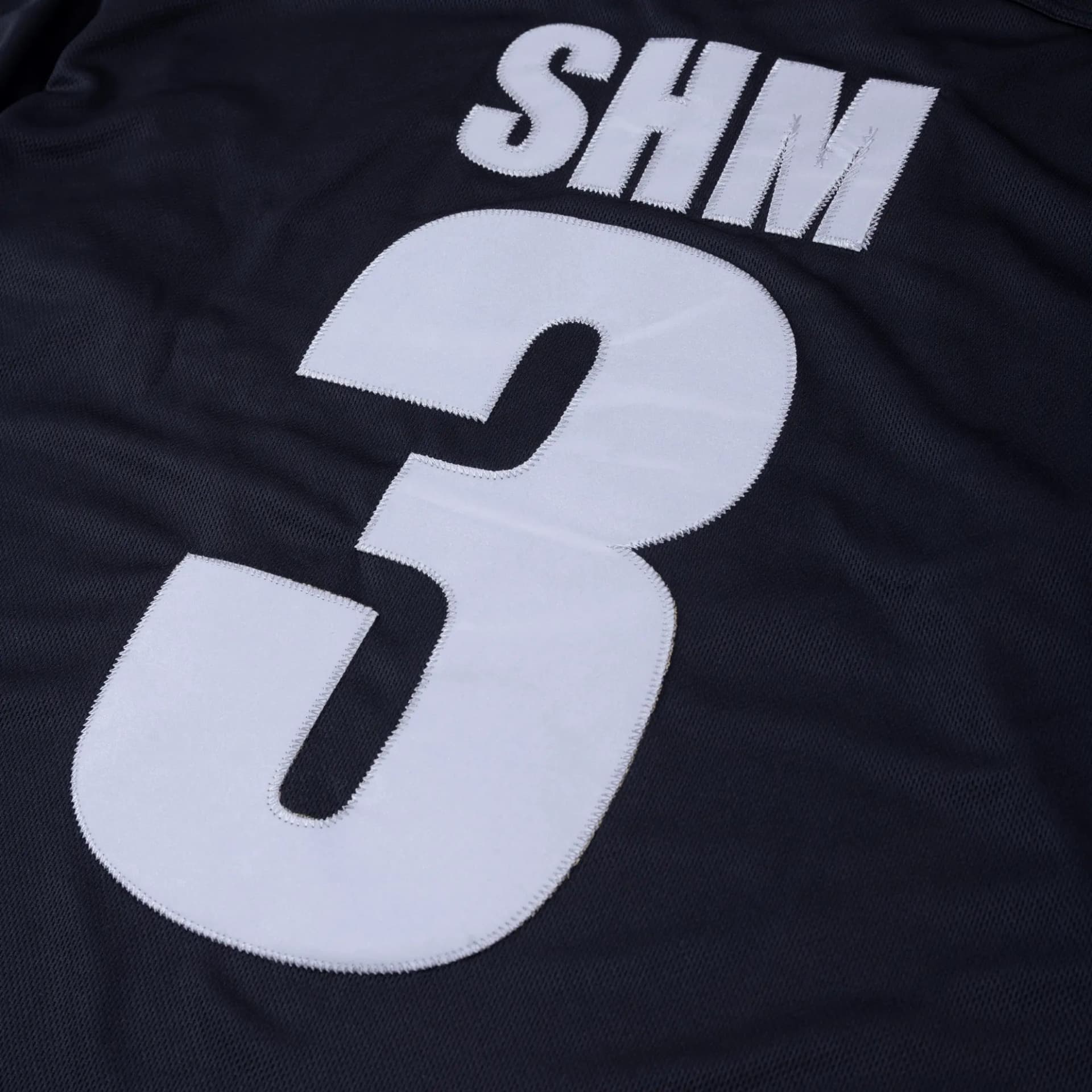 Back of the black mesh Swedish House Mafia jersey with SHM and a large number 3 in white appliqué with zigzag stitching.