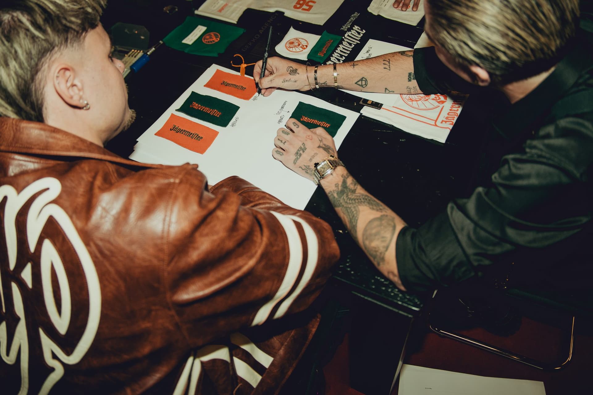 Two team members seen from above signing off embroidered Jägermeister swatches on an approval sheet, with print samples spread across the table.