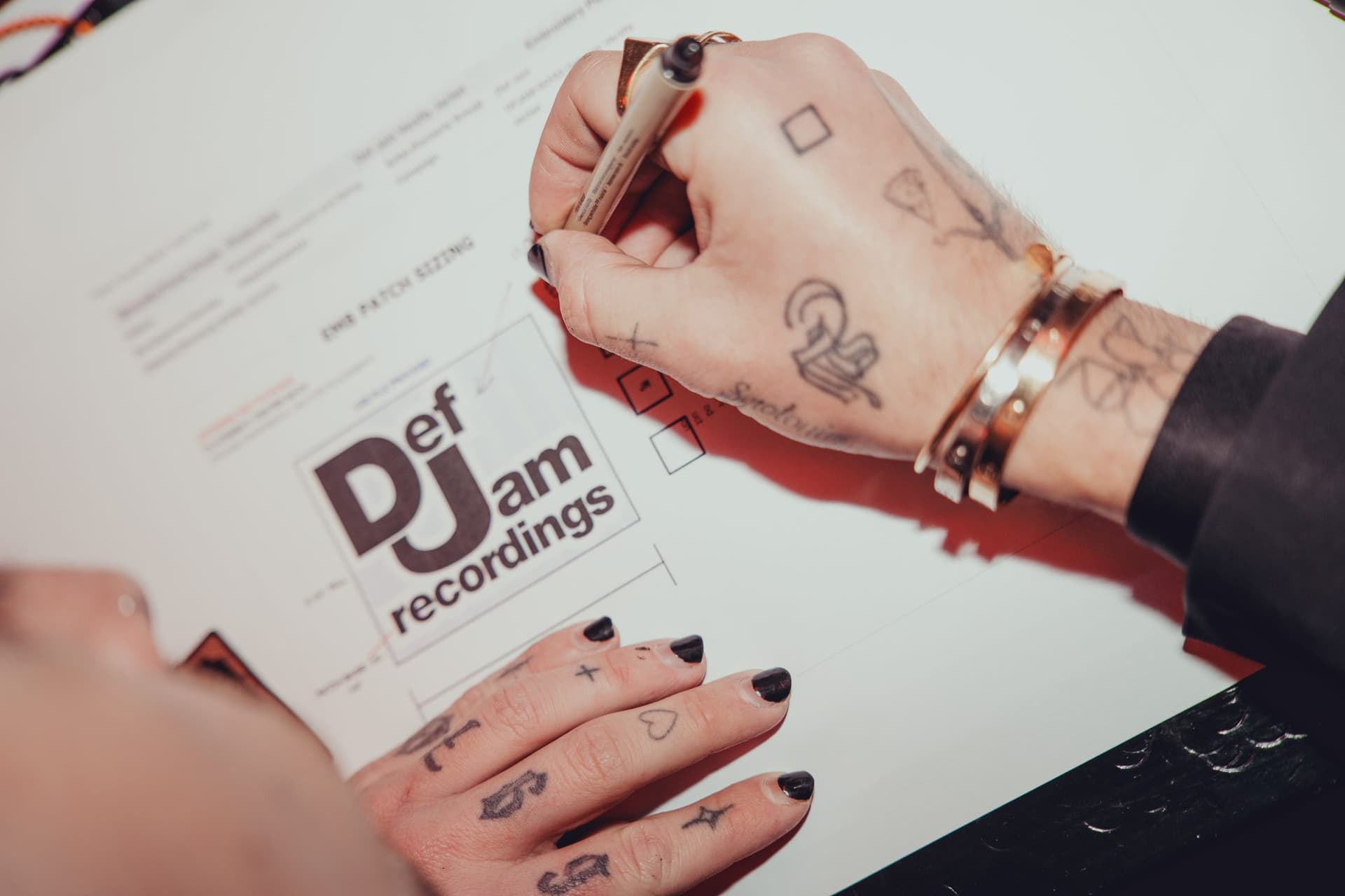 Tattooed hands with black nail polish marking up a Def Jam embroidery patch sizing sheet with a fineliner.