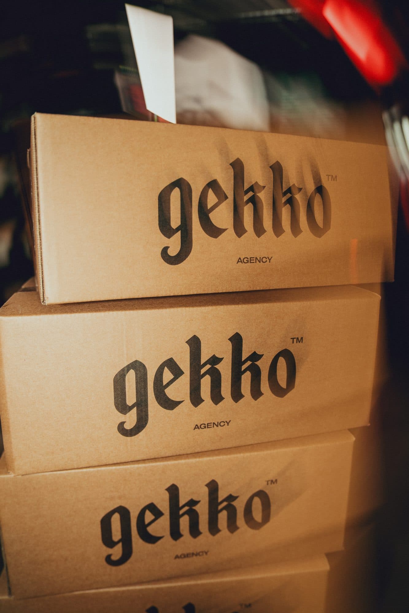 Stack of kraft shipping boxes printed with the GEKKO Agency logo in warm light.