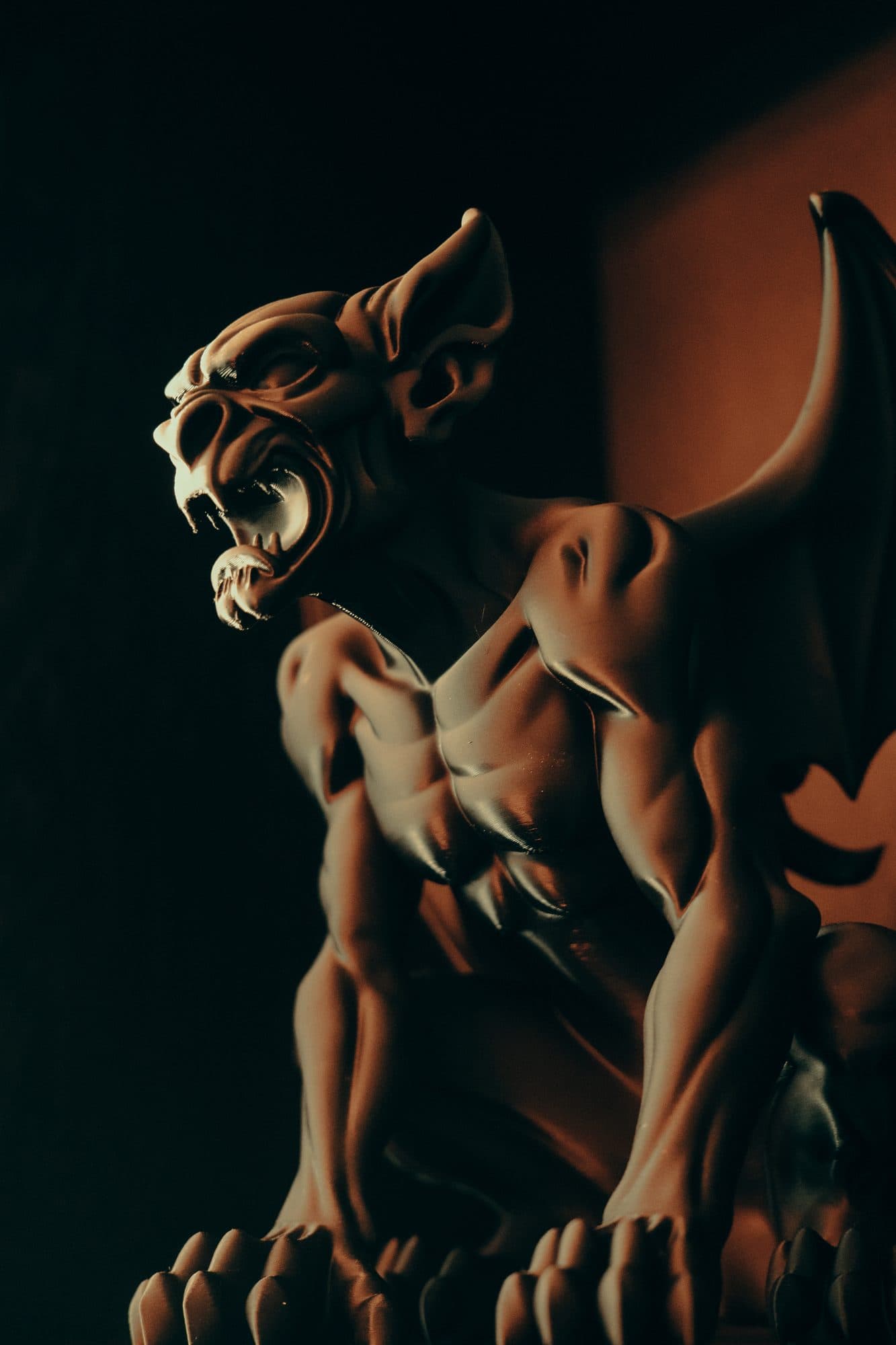 Gargoyle sculpture in warm side light against a dark background, its fine layered surface catching the light.