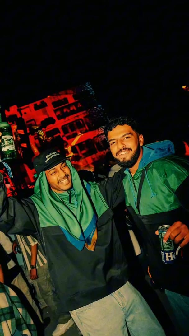 Two people at night, one in a green hood and a green and black windbreaker, the other holding a Heineken can; the film goes on to friends in the same windbreakers raising cans together, a hug and a person drinking from a can.
