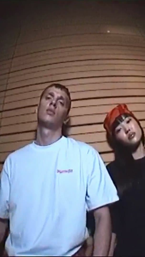 A person in a white T-shirt with small pink Jägermeister lettering beside a person in a red bandana, against a curved slatted wall at night; the film goes on to a burger in a checked paper tray, a black Jägermeister sweatshirt at a snack bar and friends clinking small green bottles.