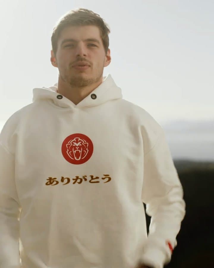 Max Verstappen on a hill above the sea in a cream hoodie with a red roundel with a lion's head and the Japanese word ありがとう on the chest; the film opens with him seen from behind and shows him pulling the hood down.